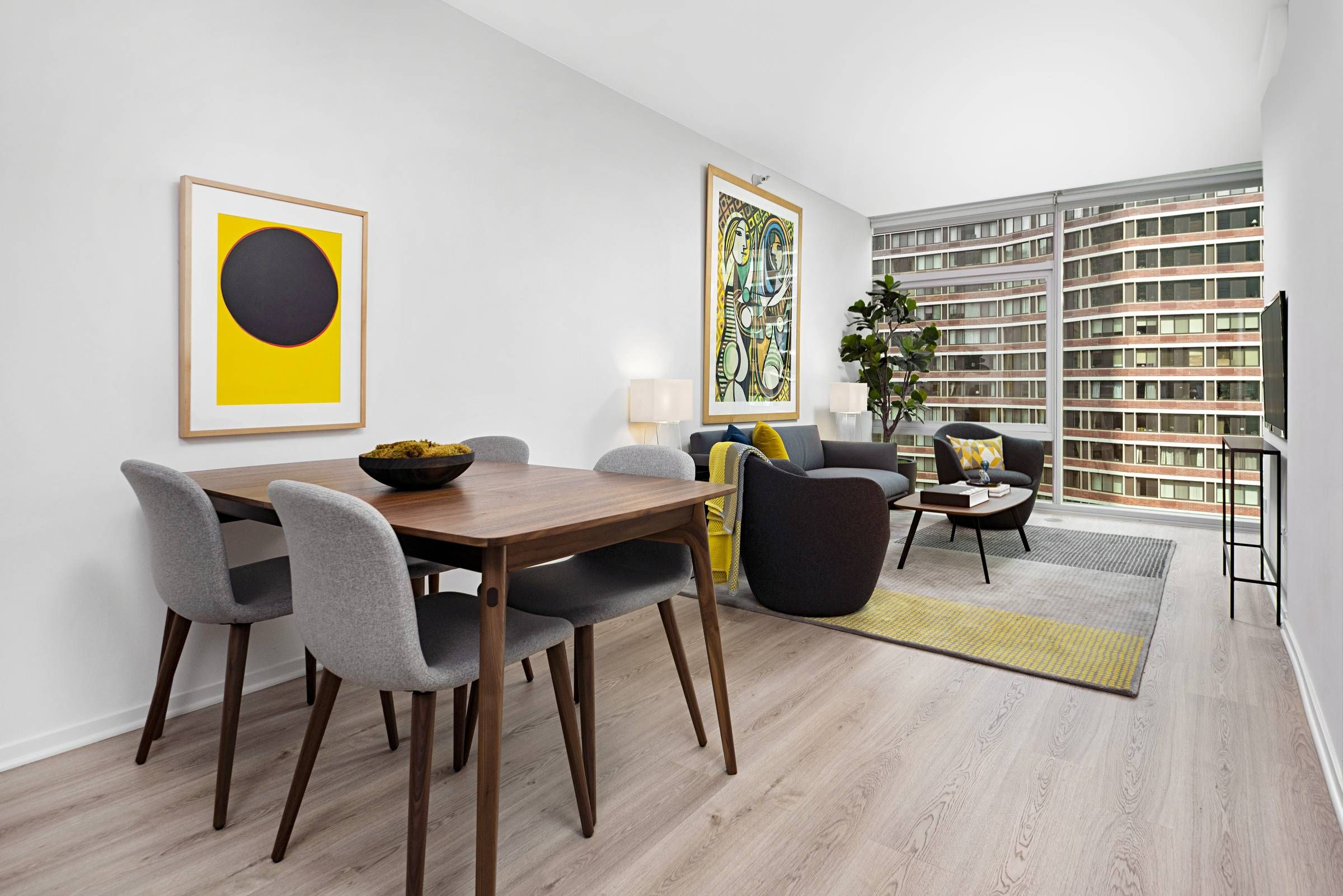 Optima Signature in Downtown Chicago with Modern living and dining area with minimalist furniture, bright artwork, and large window overlooking buildings.
