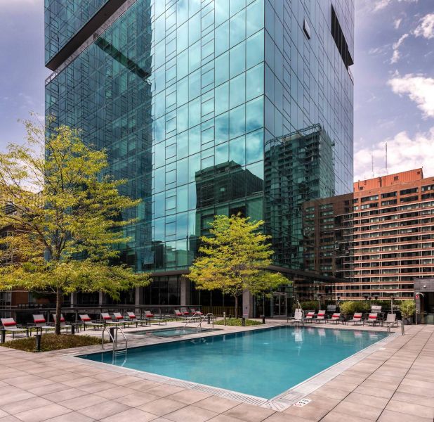 Optima Signature in Downtown Chicago with Outdoor pool with lounge chairs and trees beside a tall glass building in an urban area.