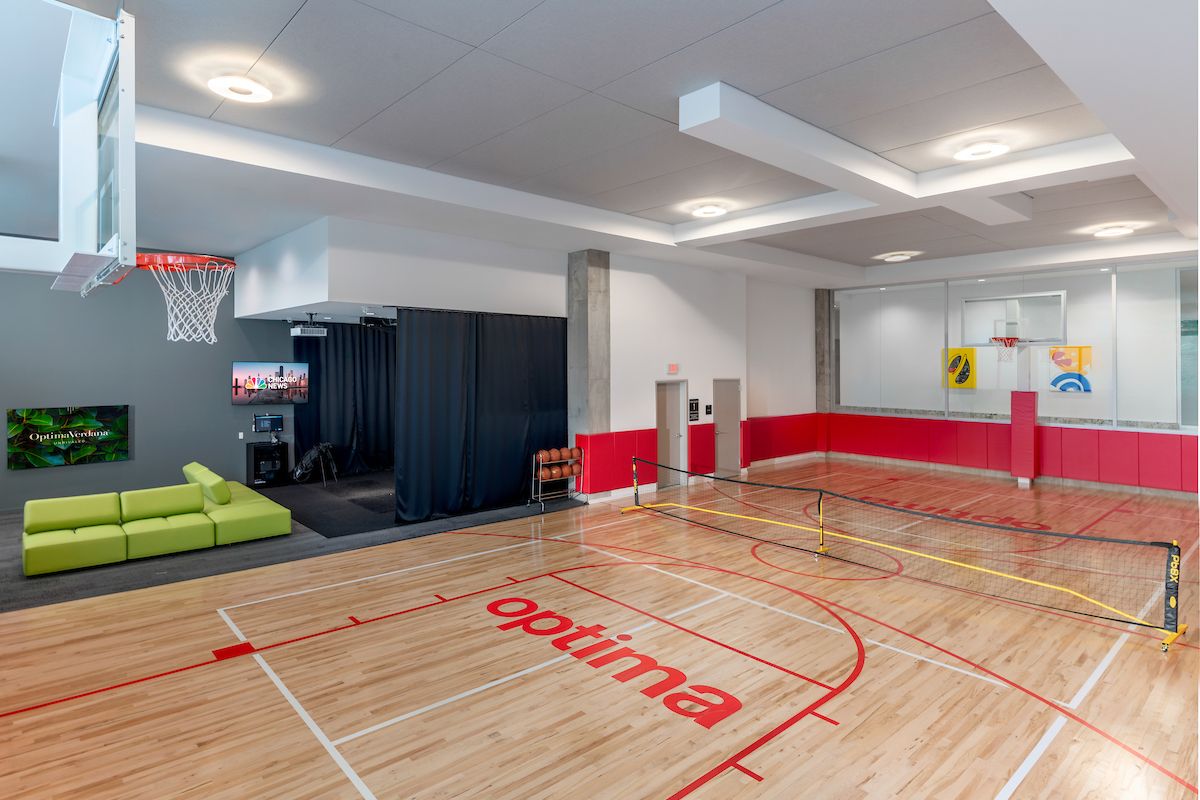 Optima Signature in Downtown Chicago with Indoor gym with a basketball court, tennis net for pickleball, green couch, TV, and red and white walls—perfect for an active lifestyle.