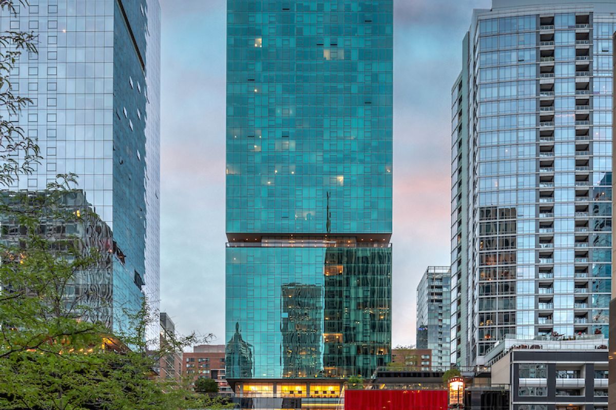 Optima Signature in Downtown Chicago with Tall glass skyscraper with red lower facade on a city street at dusk, flanked by other modern buildings.