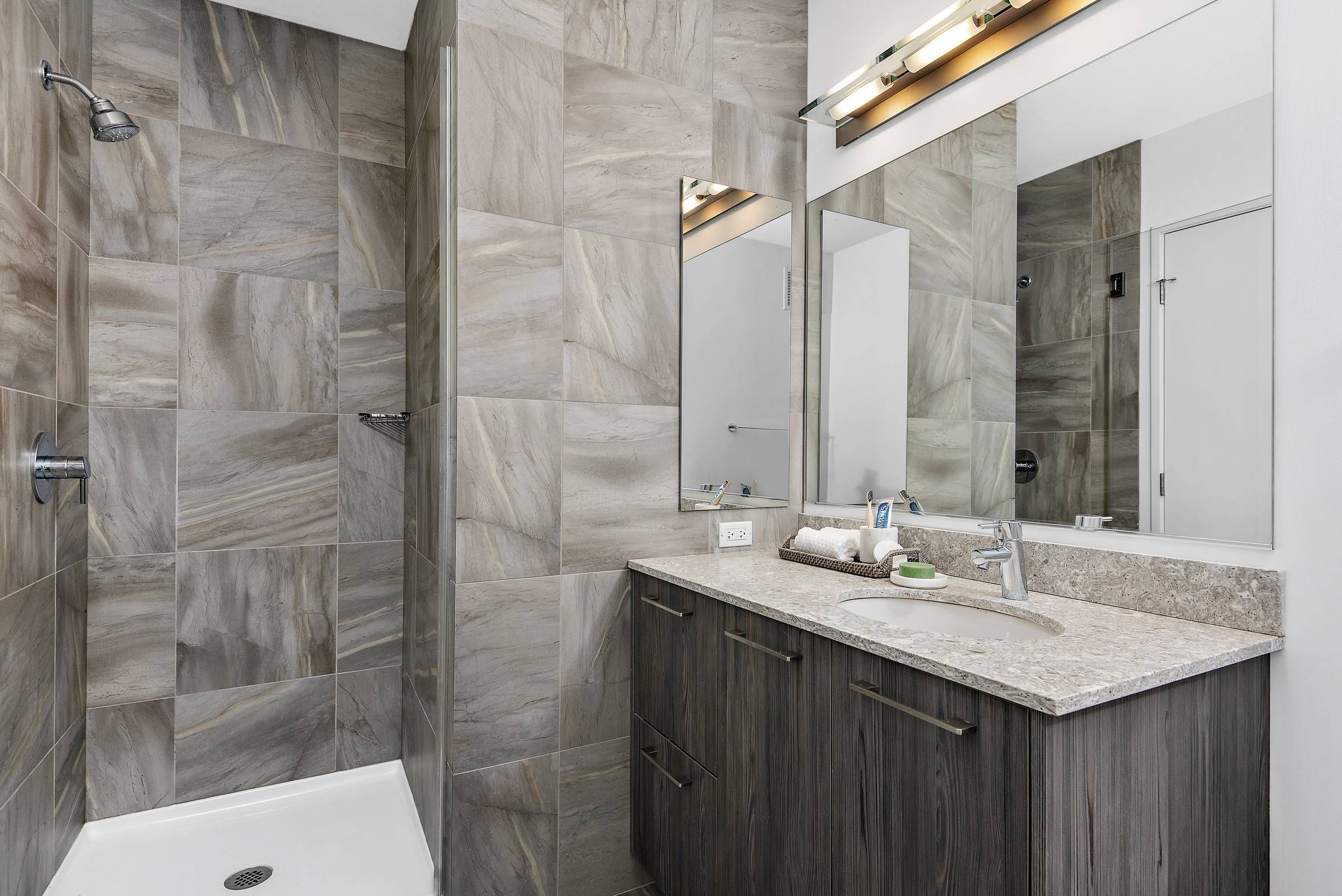 Optima Signature in Downtown Chicago with Modern bathroom with tiled shower, large mirror, and wood vanity with granite countertop and sink.