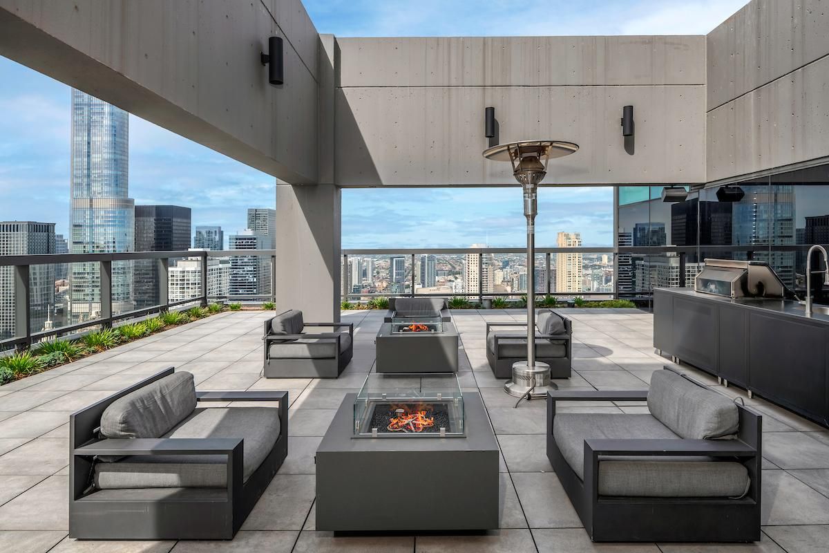 Club 52 rooftop sky deck at Optima Signature featuring modern grey seating, glass-enclosed fire pits, and panoramic views of the Chicago skyline.