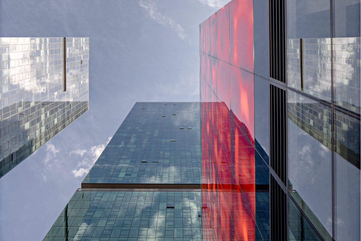 Optima Signature in Downtown Chicago with Tall glass skyscrapers from every angle, with Optima Signature’s red vertical section reflected in sky-filled windows above.