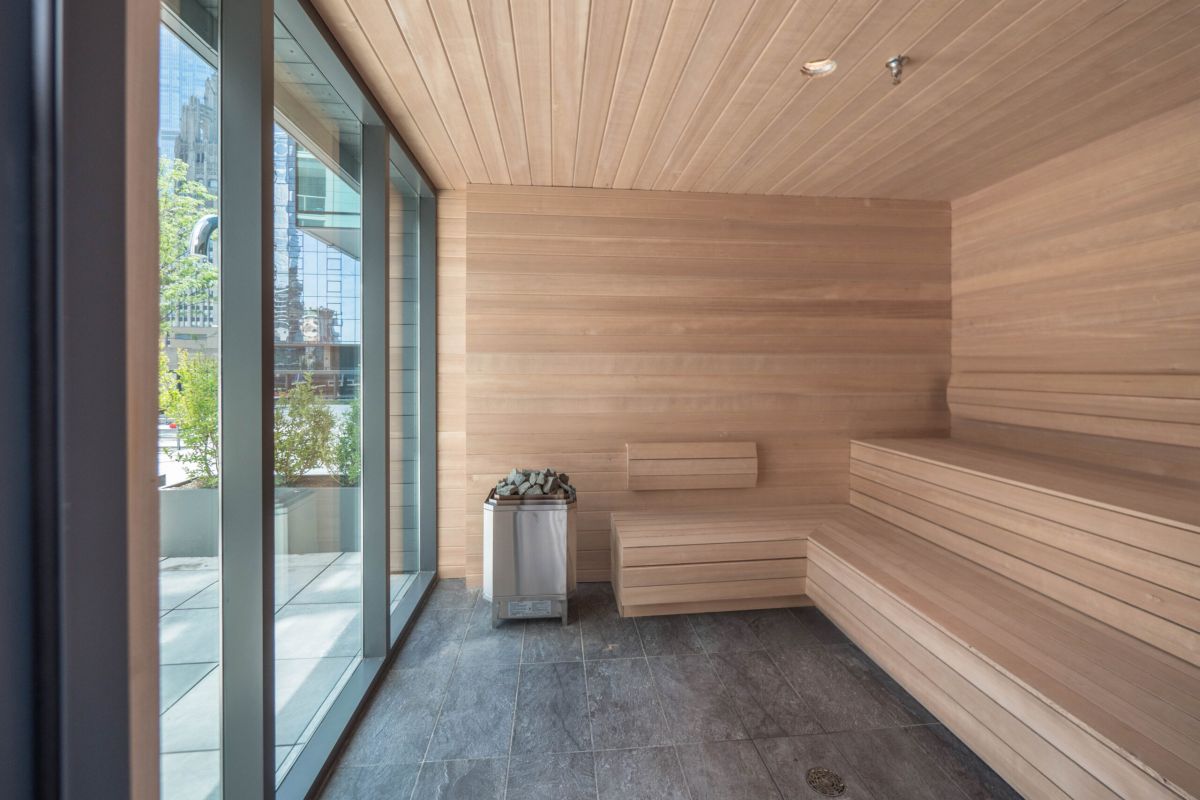 Optima Signature in Downtown Chicago with Modern wooden sauna with tiered benches, rocks heater, and Optima Signature Recovery Circuit, overlooking an urban area.