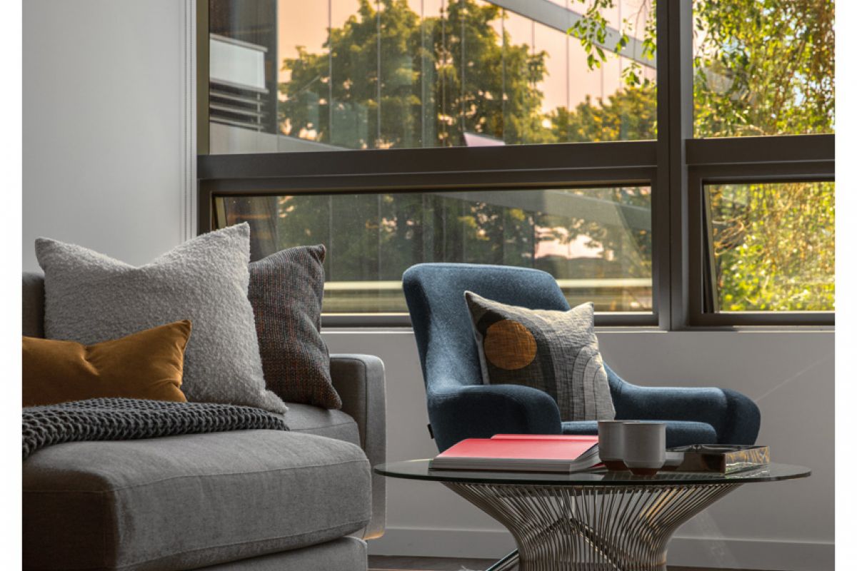 Optima Signature in Downtown Chicago with Modern living room featuring Optima furniture—a gray sofa, blue armchair, round coffee table, and large window with outdoor view.