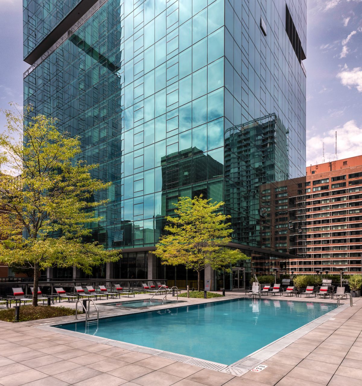 Optima Signature in Downtown Chicago with Rooftop outdoor pool with lounge chairs, surrounded by trees and city views at Optima Sky Decks on a sunny day.