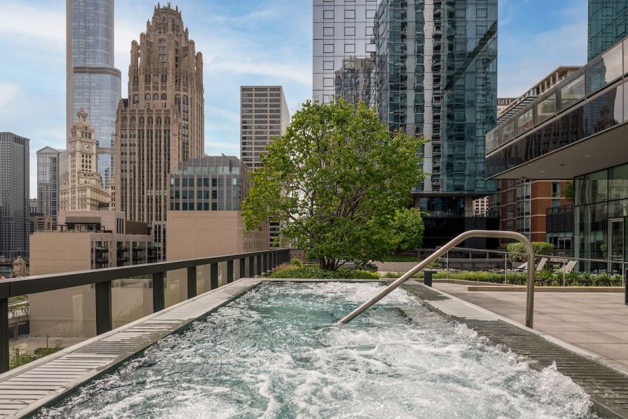 Optima Signature in Downtown Chicago with Rooftop hot tub with bubbling water, city skyscrapers, and a tree in the background on a sunny day.