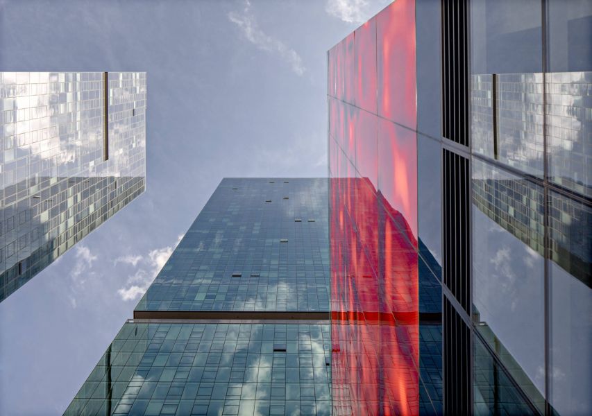 Optima Signature in Downtown Chicago with Looking up at modern glass skyscrapers against a blue sky, with red reflections on one building.