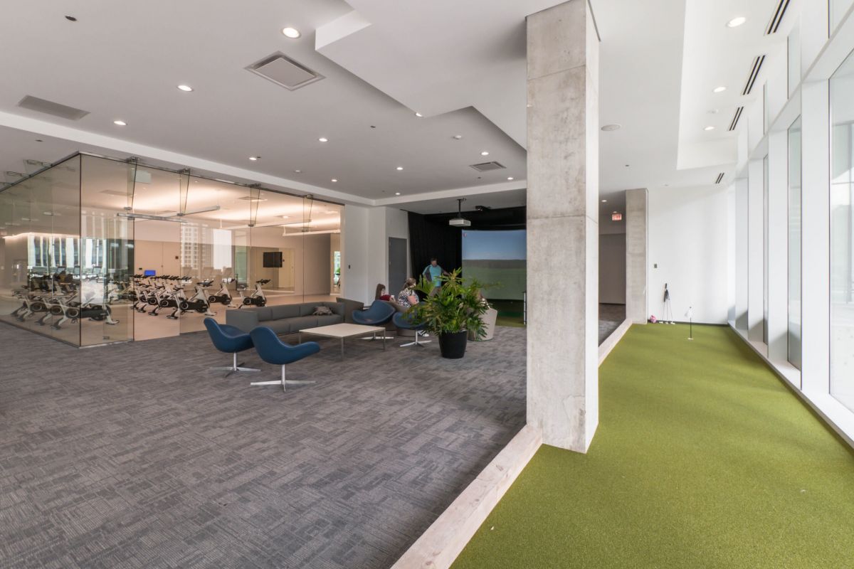 Optima Signature in Downtown Chicago with Modern office lounge with blue chairs, glass-walled meeting room, potted plants, and a virtual golf simulator for relaxation.