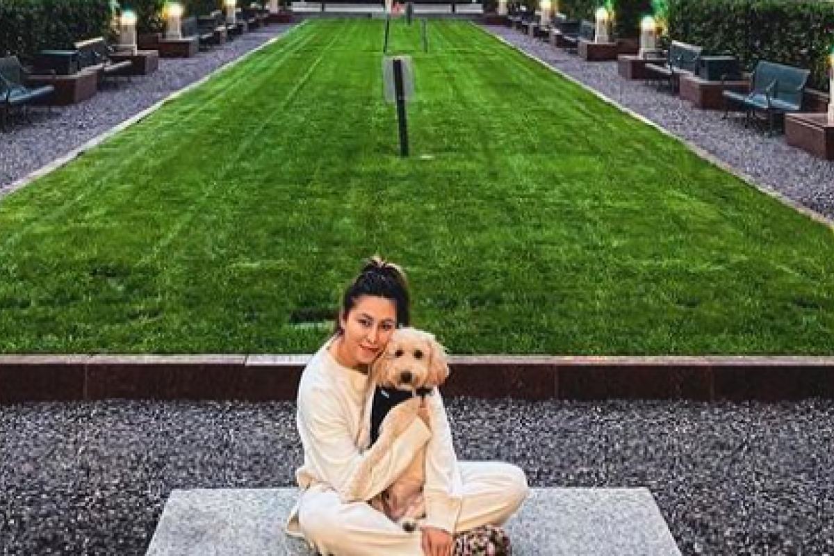 Optima Signature in Downtown Chicago with Woman in light clothes sits with her dog in a pet-friendly city park near Optima Signature, surrounded by tall glass buildings and trees.