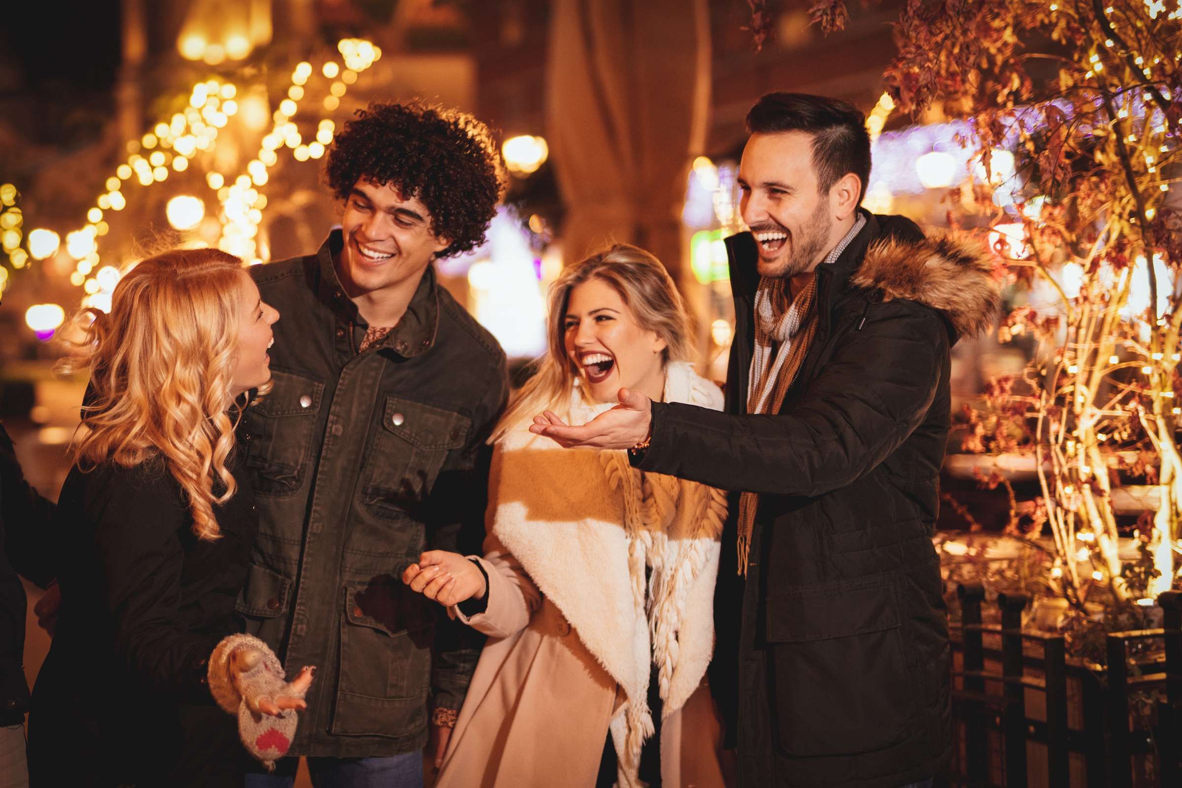 Optima Signature in Downtown Chicago with Four friends laugh together outdoors at night, surrounded by festive lights and winter clothing.