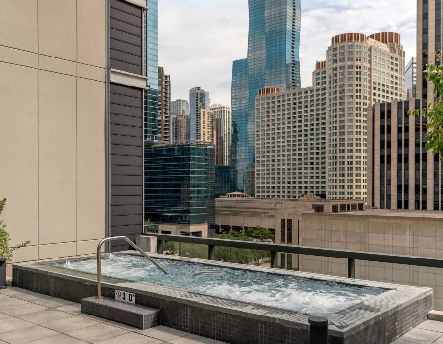 Optima Signature in Downtown Chicago with A rooftop hot tub with city skyscrapers and the Loews building in the background under a blue sky.