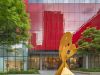 Optima Signature in Downtown Chicago with Yellow abstract sculpture by artists shines at Optima Spaces, from canvas to courtyard, framed by red reflections and green trees.
