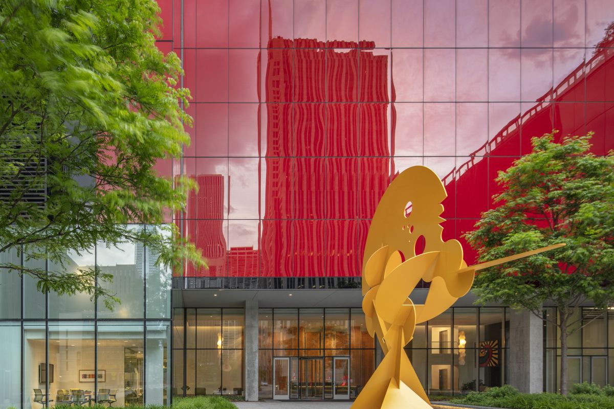 Optima Signature in Downtown Chicago with Yellow abstract sculpture by artists shines at Optima Spaces, from canvas to courtyard, framed by red reflections and green trees.