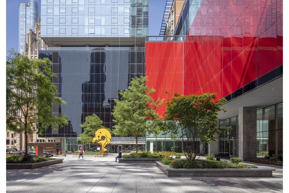 Optima Signature in Downtown Chicago with Modern city plaza with trees, Art, a yellow abstract sculpture, and glass buildings—one with a bold red facade and Optima's Lobbies.