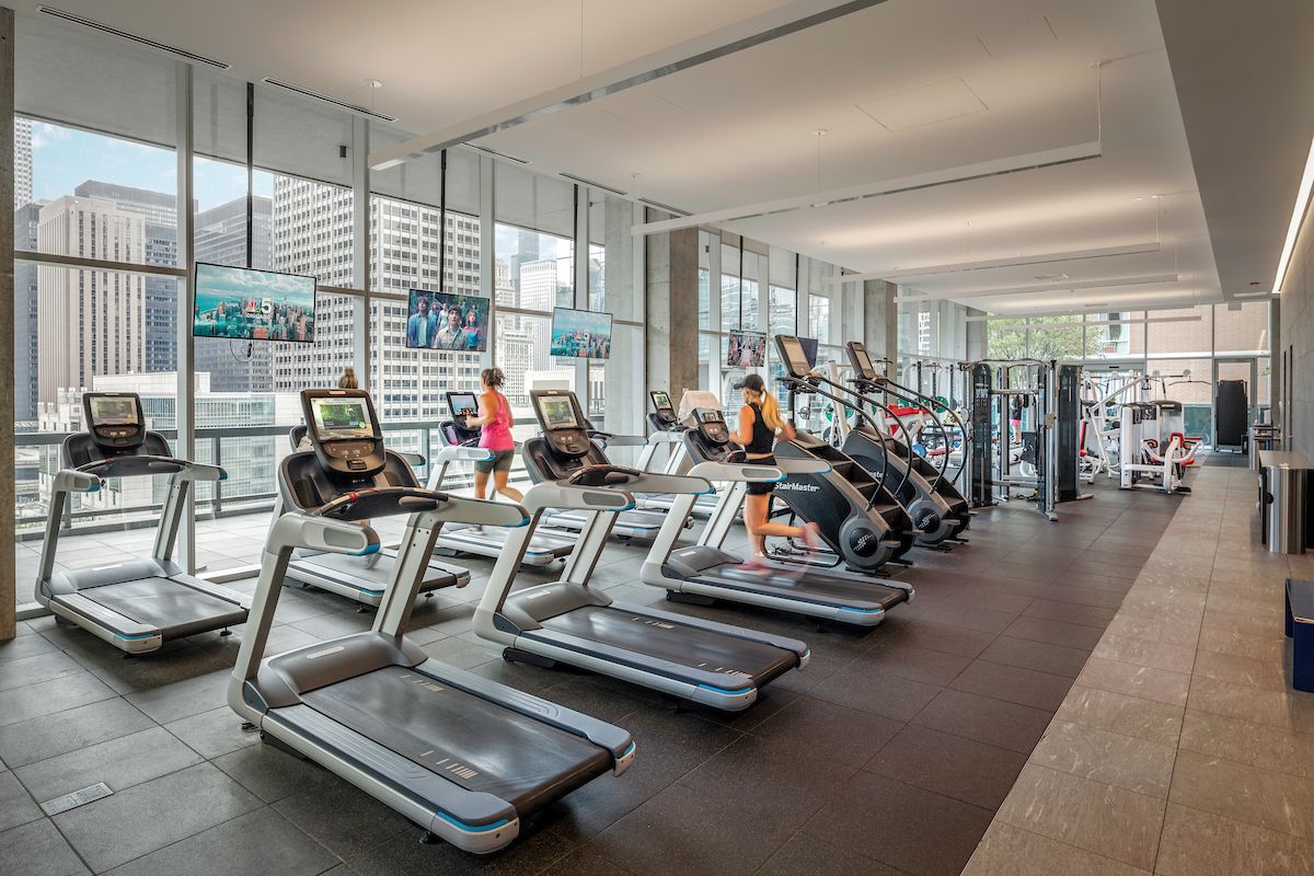 Optima Signature in Downtown Chicago with Modern gym with treadmills, ellipticals, and people exercising; large windows show city buildings outside.