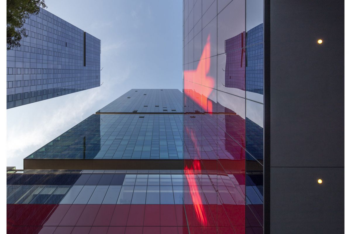 Optima Signature in Downtown Chicago with A low-angle view of modern glass buildings with red reflections and a blue sky above, reflecting the spirit of Optima Community.