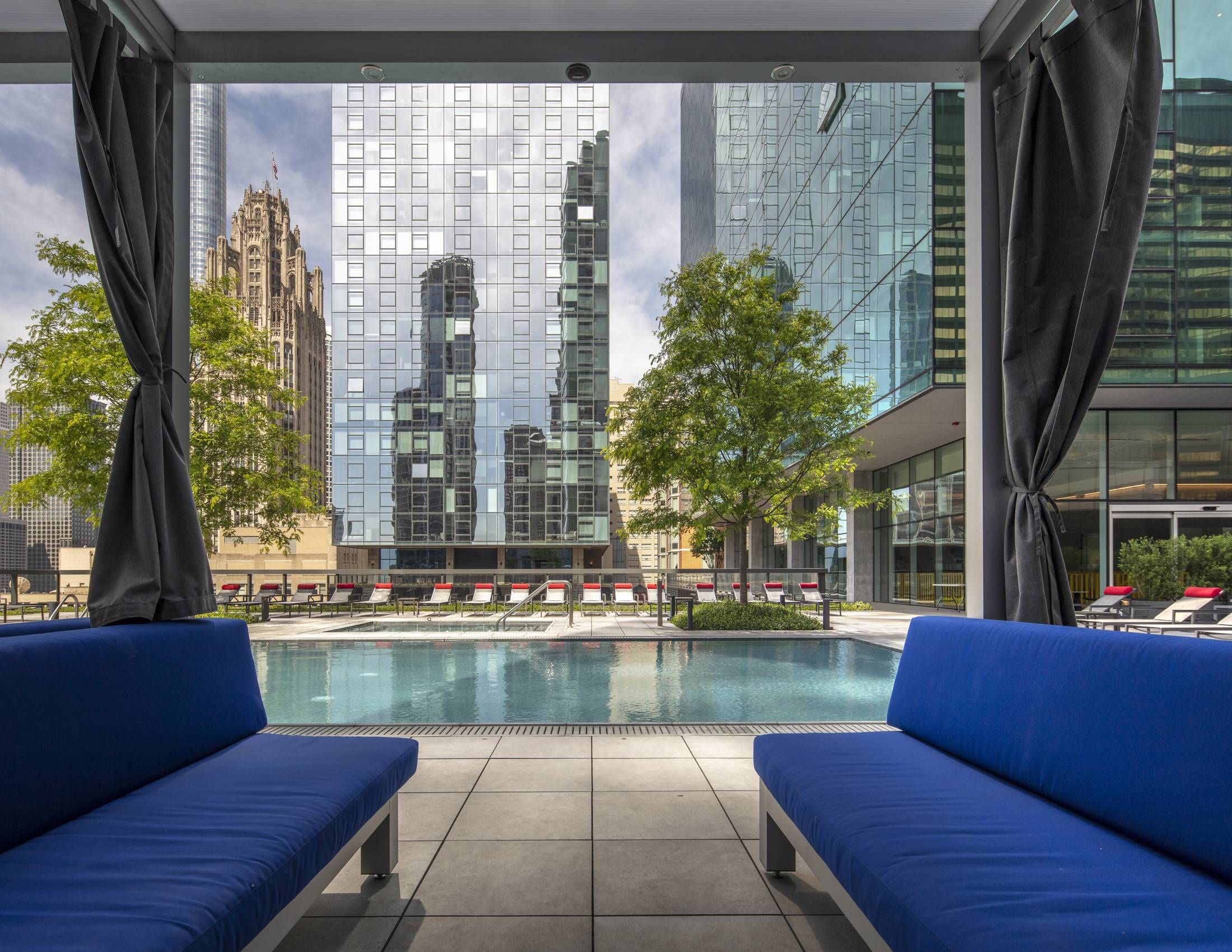Optima Signature in Downtown Chicago with View of a city pool surrounded by modern buildings, seen from between two blue benches under a canopy.