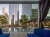Optima Signature in Downtown Chicago with Modern pool area with blue seating, surrounded by tall glass buildings and trees, viewed from under a shaded canopy.