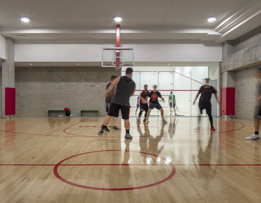 Optima Signature in Downtown Chicago with Five people play basketball on an indoor court with wooden floors; a person watches from behind glass.