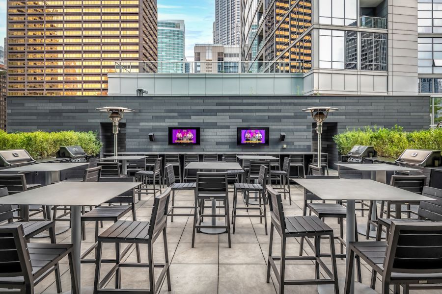 Optima Signature in Downtown Chicago with Modern rooftop patio with tables, chairs, grills, outdoor TVs, and city skyscrapers in the background.