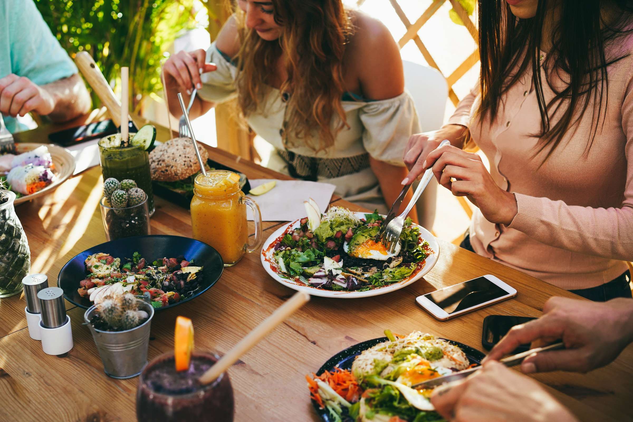 Optima Signature in Downtown Chicago with People eating salads and various dishes together at a wooden table outdoors, with drinks and phones nearby.