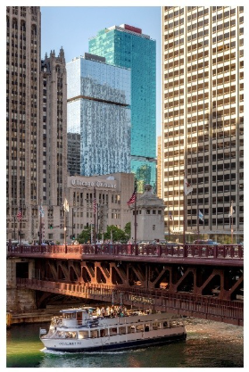 Optima Signature in Downtown Chicago with A tour boat passes under a bridge on the Chicago River, surrounded by tall city buildings.