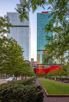 Optima Signature in Downtown Chicago with Tall glass buildings and a vibrant red structure behind a green park with trees and a sidewalk in the foreground.