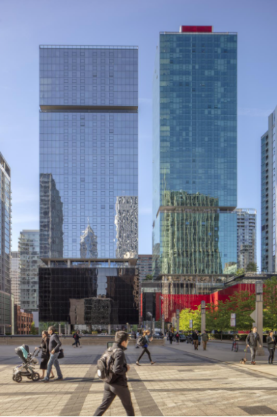 Optima Signature in Downtown Chicago with People walking in a city plaza with tall modern glass skyscrapers in the background on a sunny day.