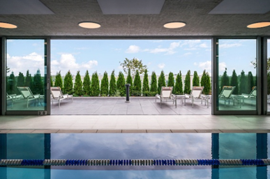 Optima Signature in Downtown Chicago with Indoor pool with lane marker, glass doors open to patio on Optima Sky Decks with lounge chairs, green trees, and city views under a blue sky.