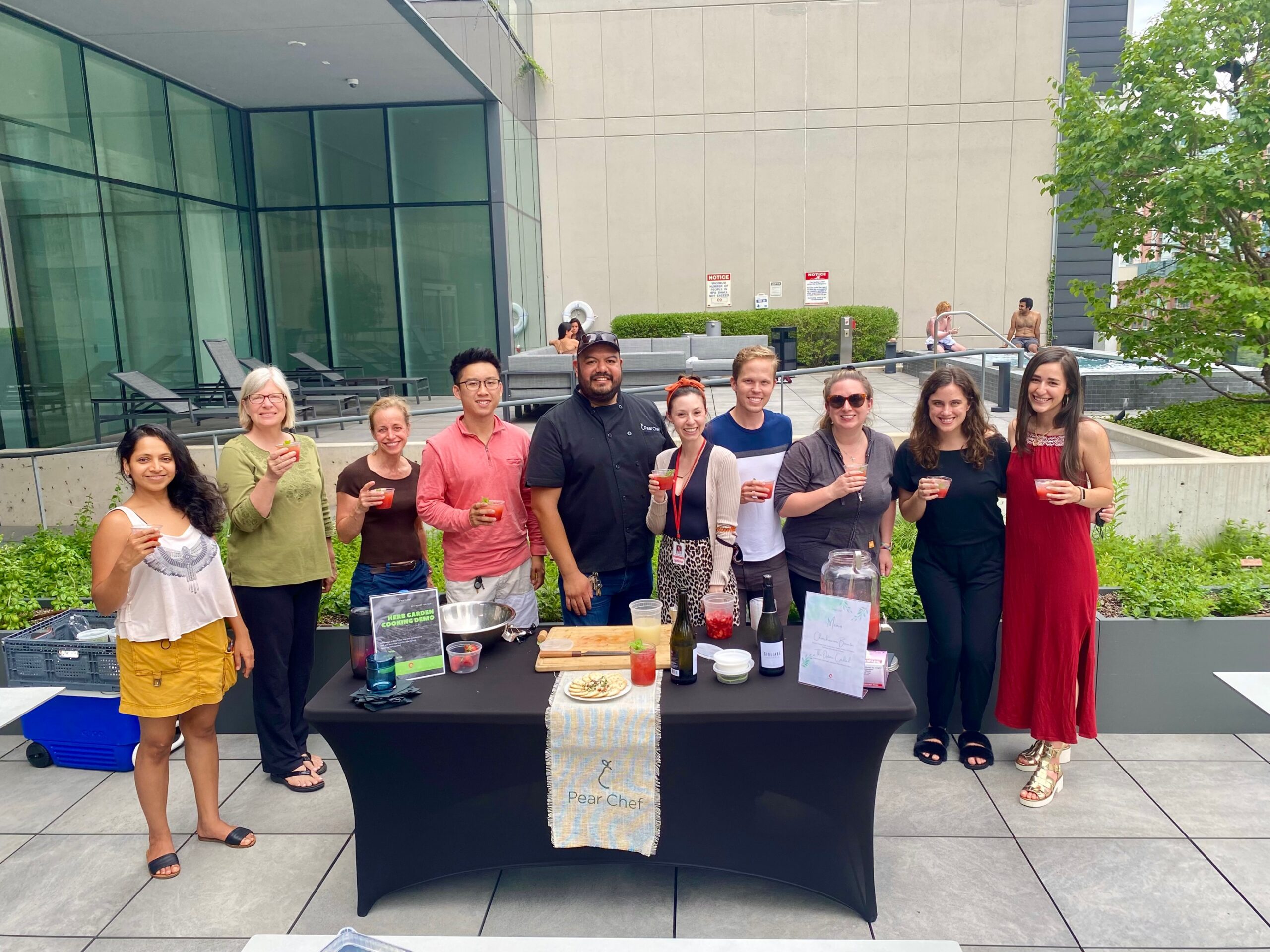 Optima Signature in Downtown Chicago with A group of people stand behind a table outdoors, smiling and holding drinks at an Optima Communities rooftop celebration event.