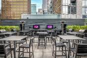 Optima Signature in Downtown Chicago with Rooftop patio with empty tables and chairs, city skyscrapers behind—perfect for Hosting at Home with two screens at the front.