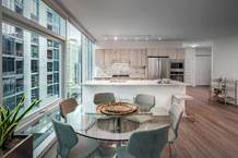 Optima Signature in Downtown Chicago with Modern apartment perfect for Hosting at Home, featuring large windows, a glass dining table, and a sleek white kitchen with stainless steel appliances.