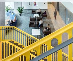 Optima Signature in Downtown Chicago with People sit and talk in a modern lounge area behind a yellow staircase, with plants and artwork visible.
