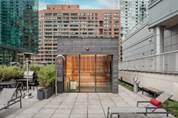 Optima Signature in Downtown Chicago with Rooftop patio with lounge chairs, potted plants, and glass doors, surrounded by tall city buildings.