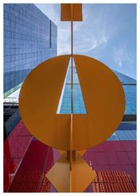 Optima Signature in Downtown Chicago with Large yellow abstract sculpture in front of modern blue and red glass buildings, viewed from below against the sky.