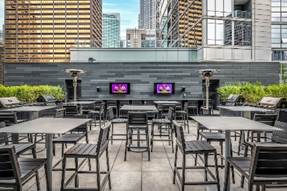 Optima Signature in Downtown Chicago with Modern rooftop patio with black tables and chairs, flat-screen TVs, and city skyscrapers in the background.