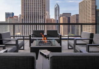 Optima Signature in Downtown Chicago with Four gray chairs surround a fire pit on a balcony with a city skyline view in the background.