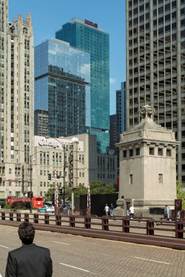 Optima Signature in Downtown Chicago with A person in a suit stands on a city street facing the Chicago Water Tower and surrounding skyscrapers.