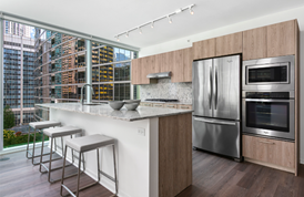 Optima Signature in Downtown Chicago with Modern kitchen with wood cabinetry, stainless steel appliances, and an island with three stools overlooking a city view.